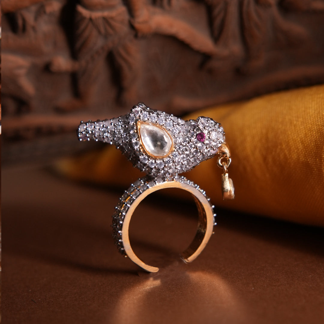 Sharanya Ring by Vasundhara, bird-shaped design with kundan and diamond accents, styled on a rich brown and gold backdrop.