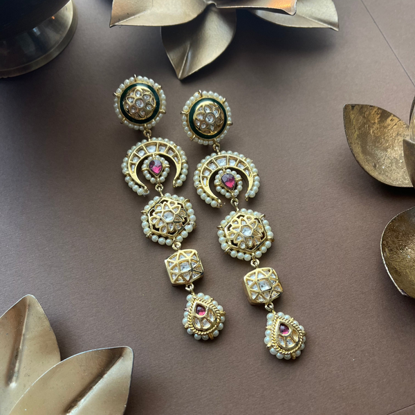 Intricate Vasundhara Hira Earrings with kundan, pearls, and ruby highlights, displayed on a background with brass decor.