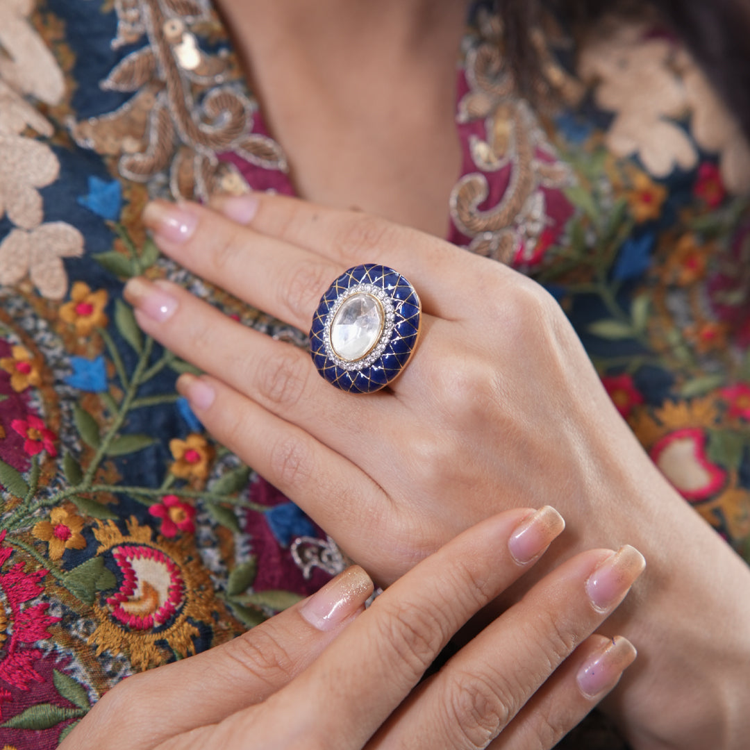 A graceful hand displays the Vasundhara Saanjh Ring, rich blue enamel encircling a crystal-edged mirror stone in soft light.