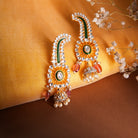 Suhani Earrings by Vasundhara with floral kundan design, pink bead accents, and pearl drops, set on yellow silk.