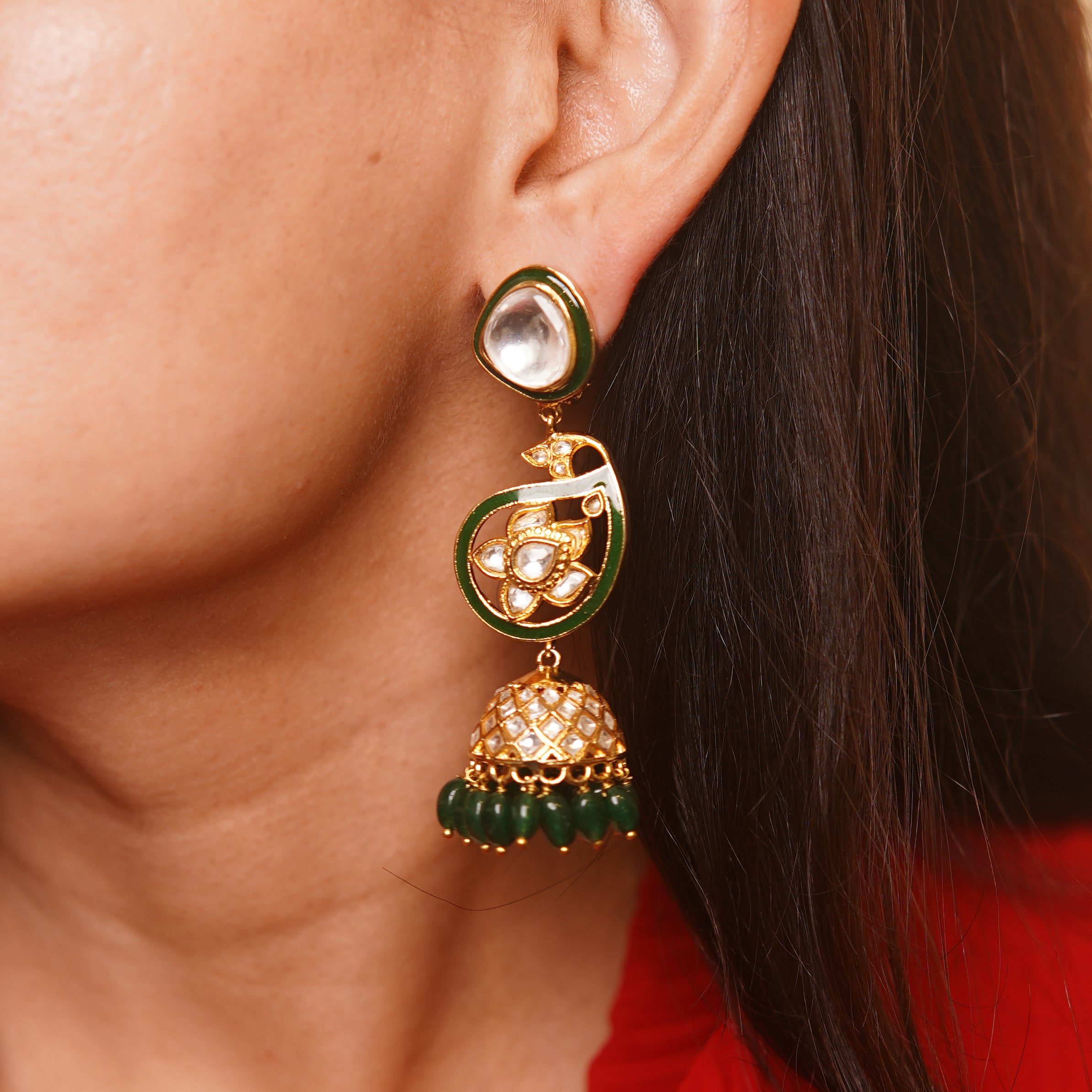 Close-up of traditional gold earrings with green enamel, kundan work, and jade beads worn on a woman's ear.