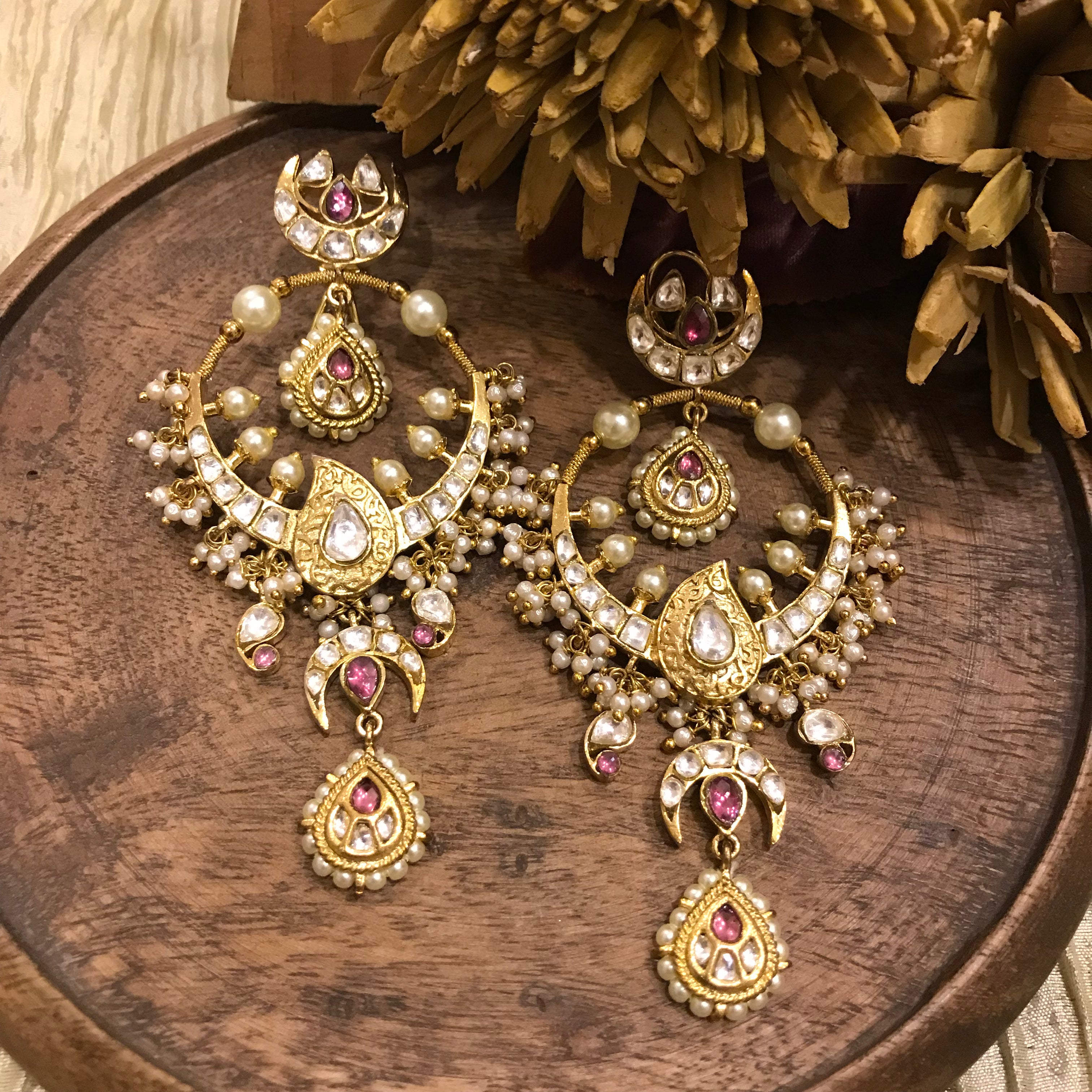 Masuma Earrings by Vasundhara, handcrafted in gold with pearls, kundan work, and pink gemstones, displayed on a wooden base.