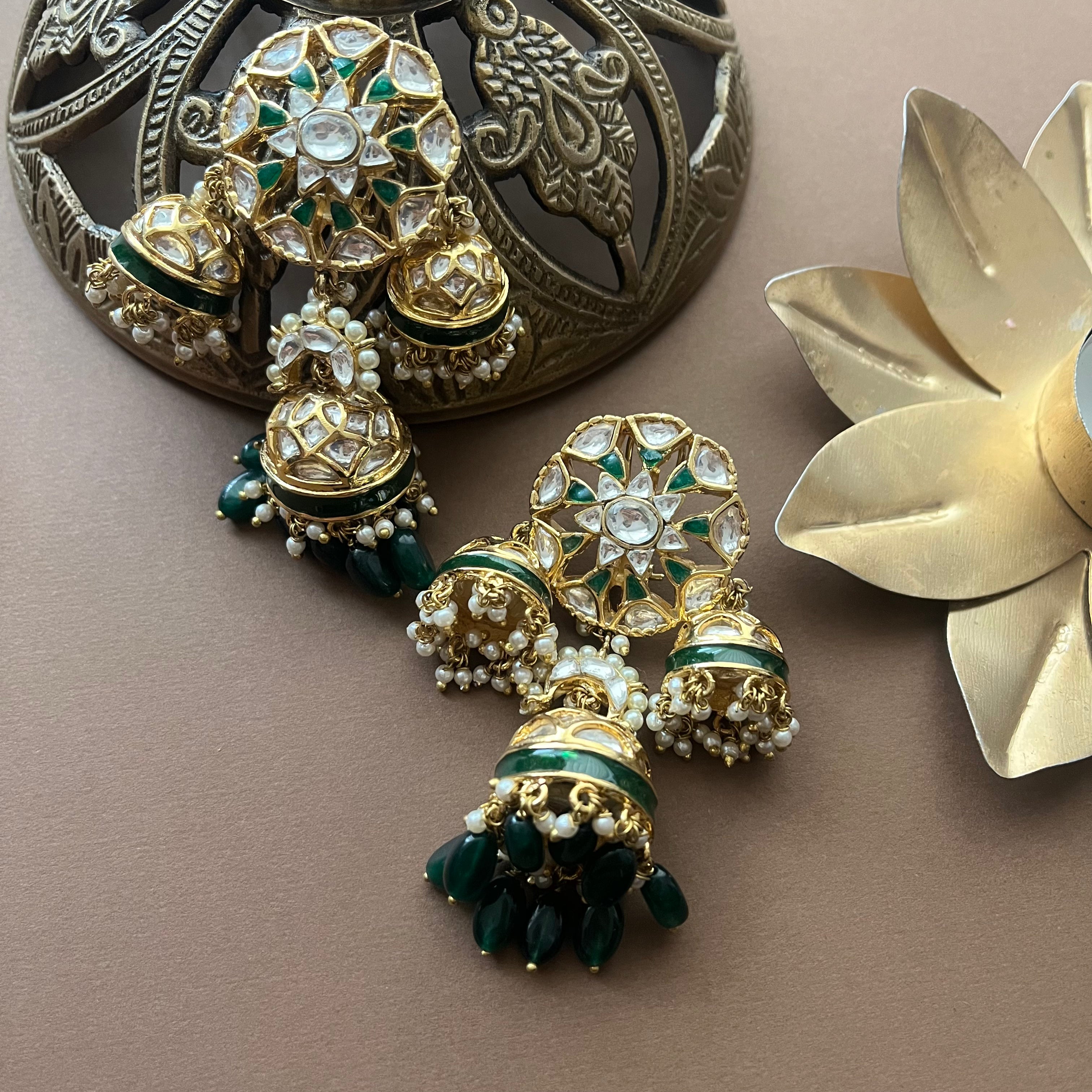 Pair of traditional gold dome-shaped kundan earrings with green beads and pearls, placed near vintage décor.