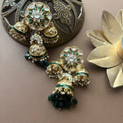 Pair of traditional gold dome-shaped kundan earrings with green beads and pearls, placed near vintage décor.
