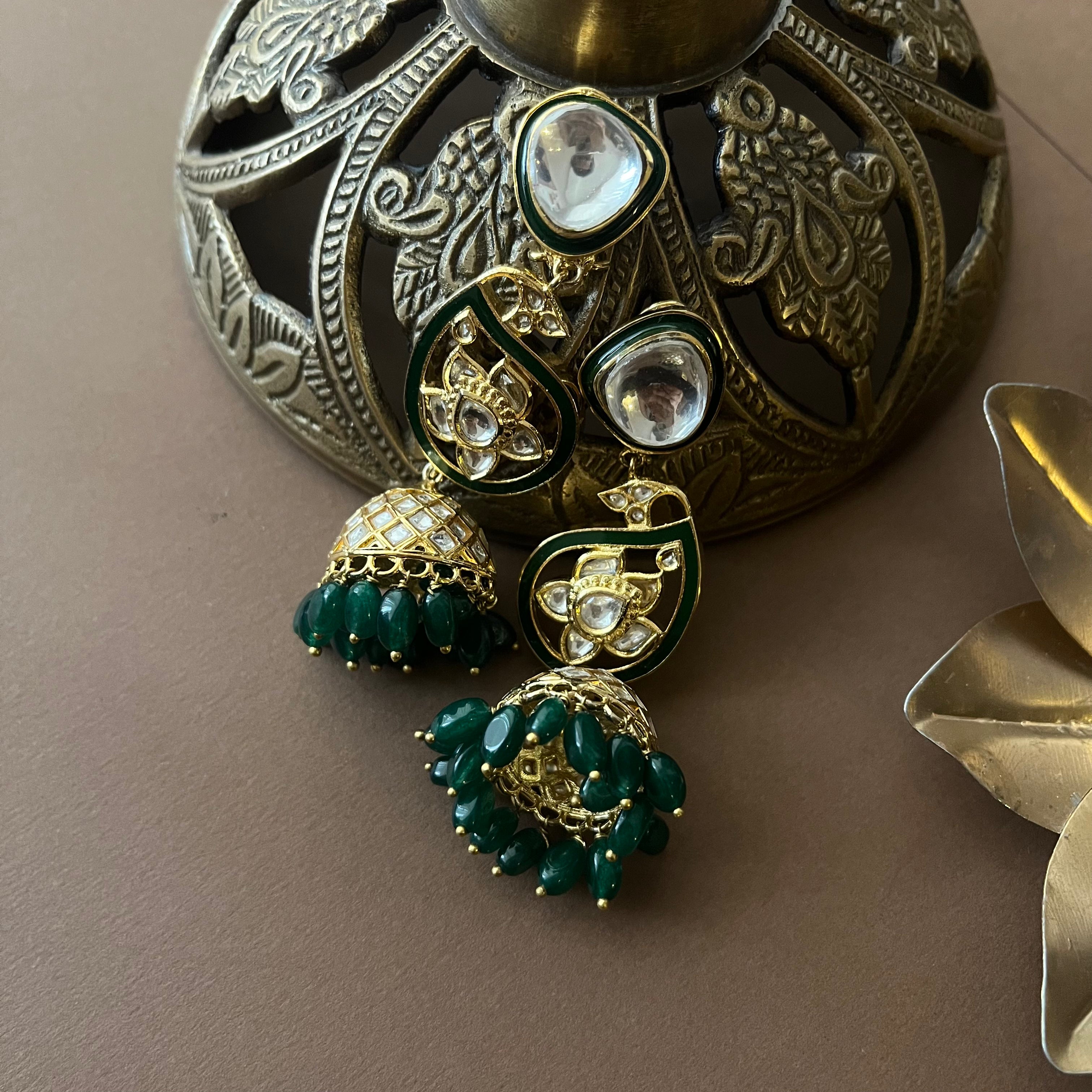 Statement ethnic earrings featuring enamel accents and jhumkas, styled with traditional brass decor props.