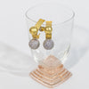 Pair of sculptural earrings with textured gold elements and pave crystal spheres, displayed against a glass