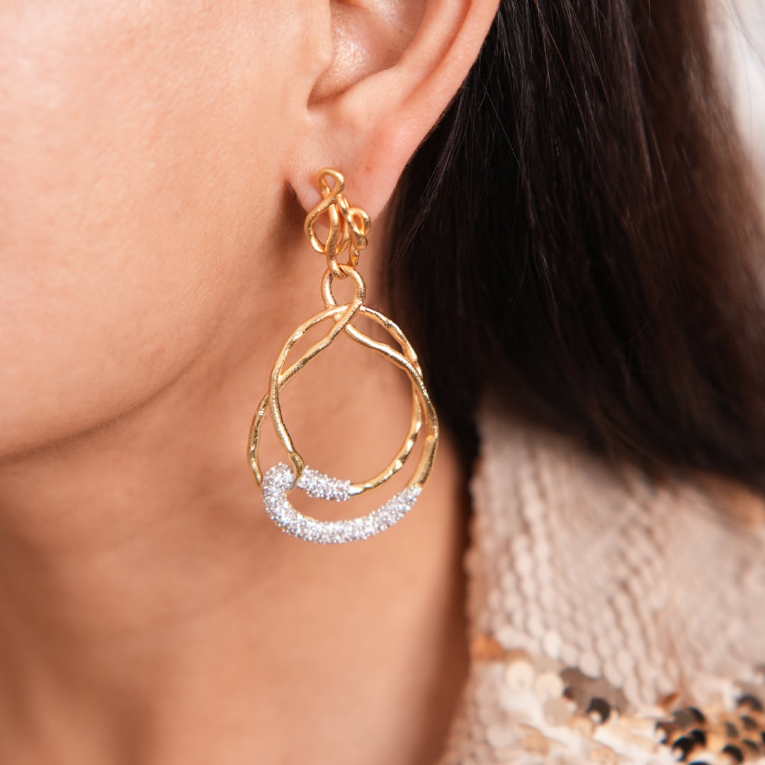 Close-up of Backstage Earring worn by a woman, showcasing gold loops and sparkling crystals in a refined teardrop design.